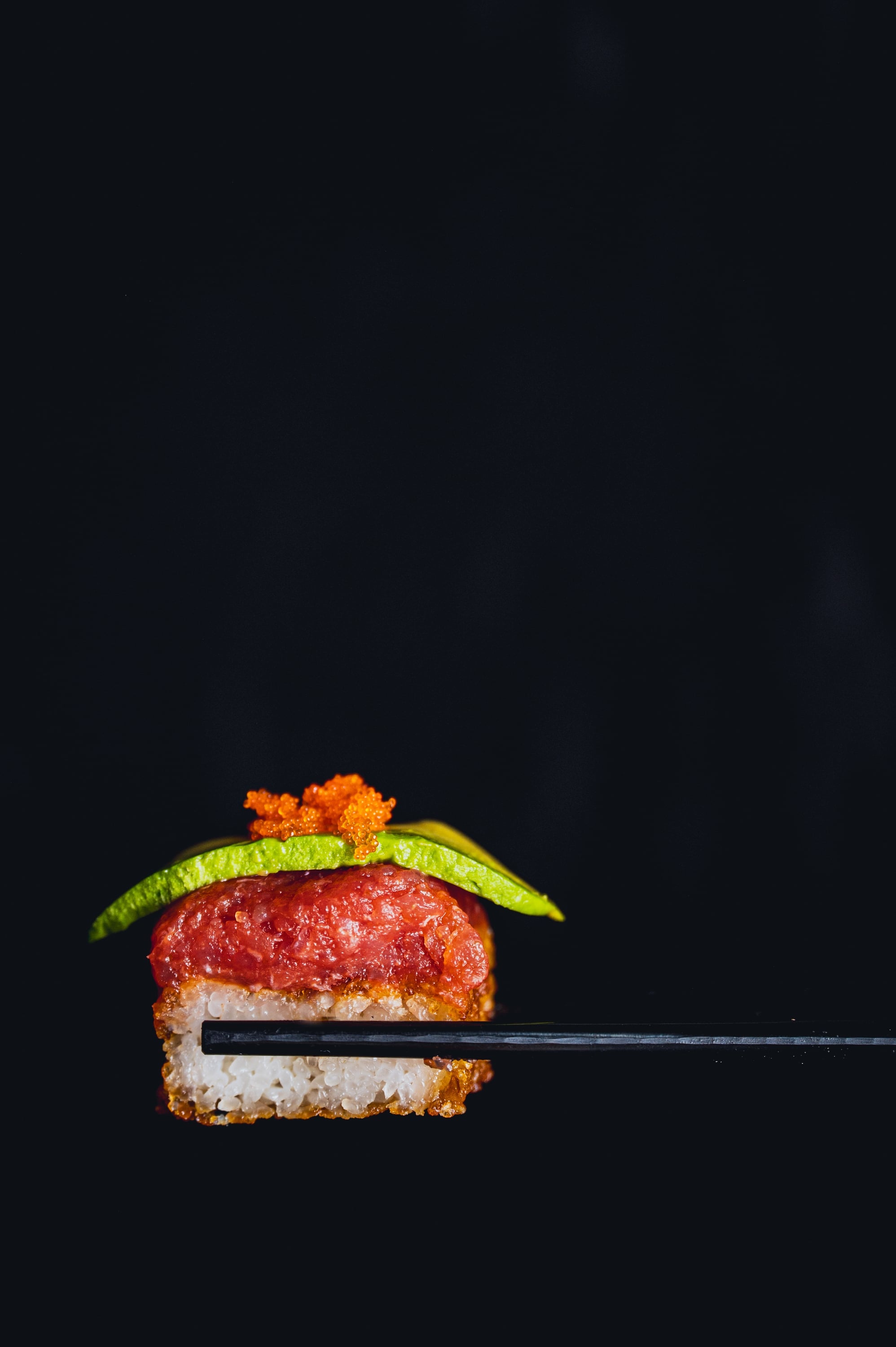 Aburi sushi with tuna and avocado held in chopsticks