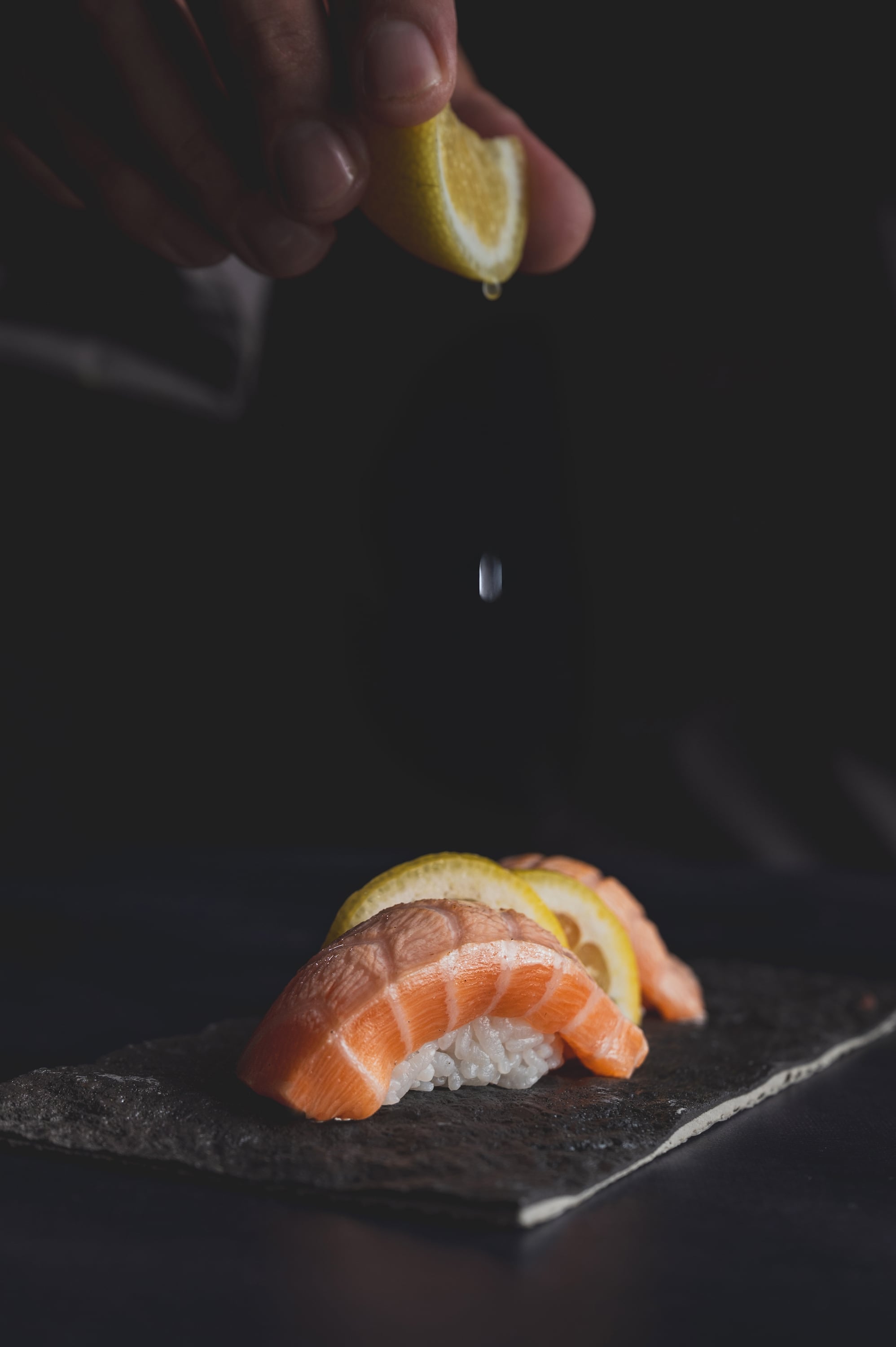 Chef's hand squeezing lemon over salmon nigiri