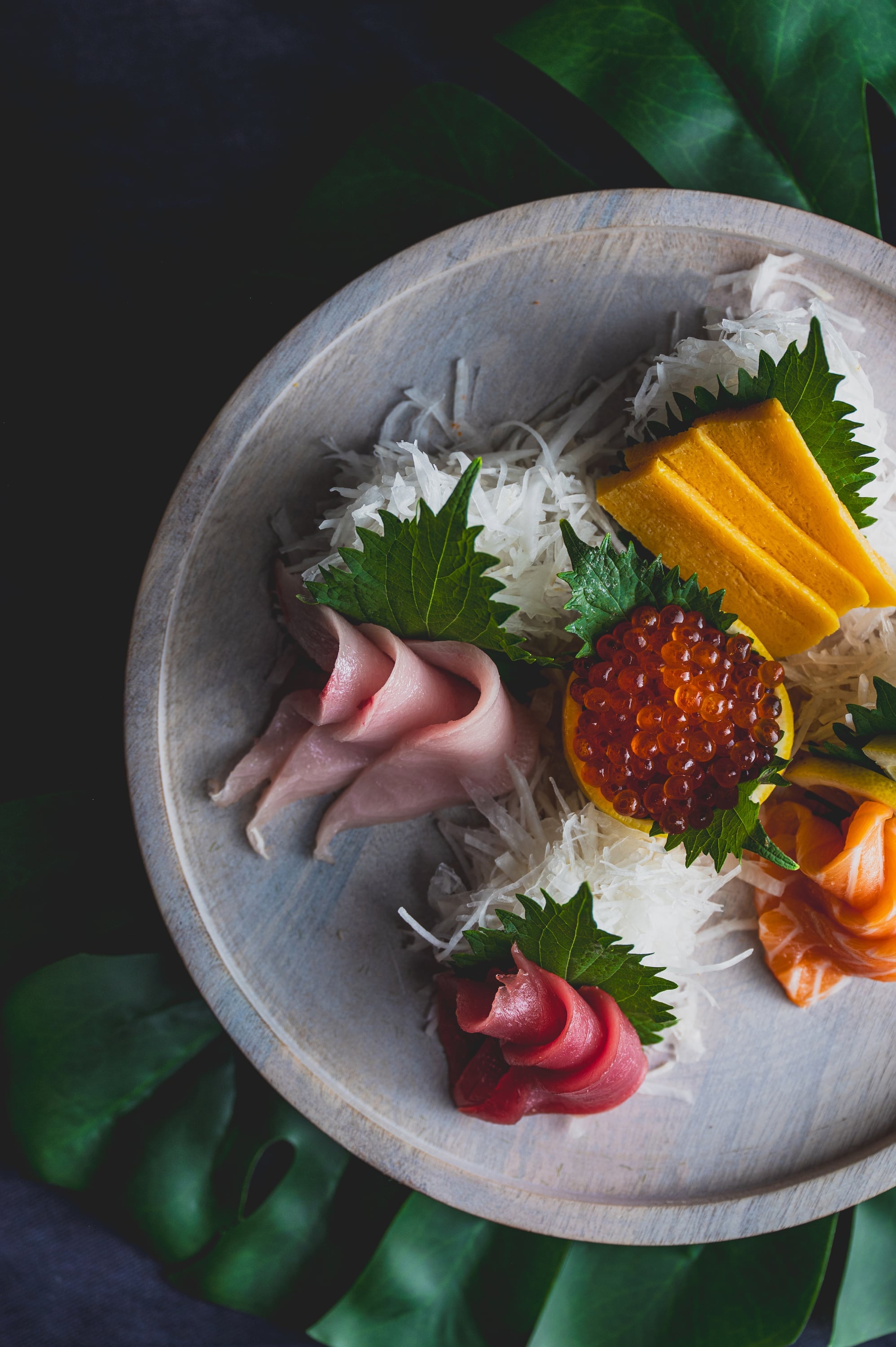 Sashimi platter on wooden plate with monstera leaves