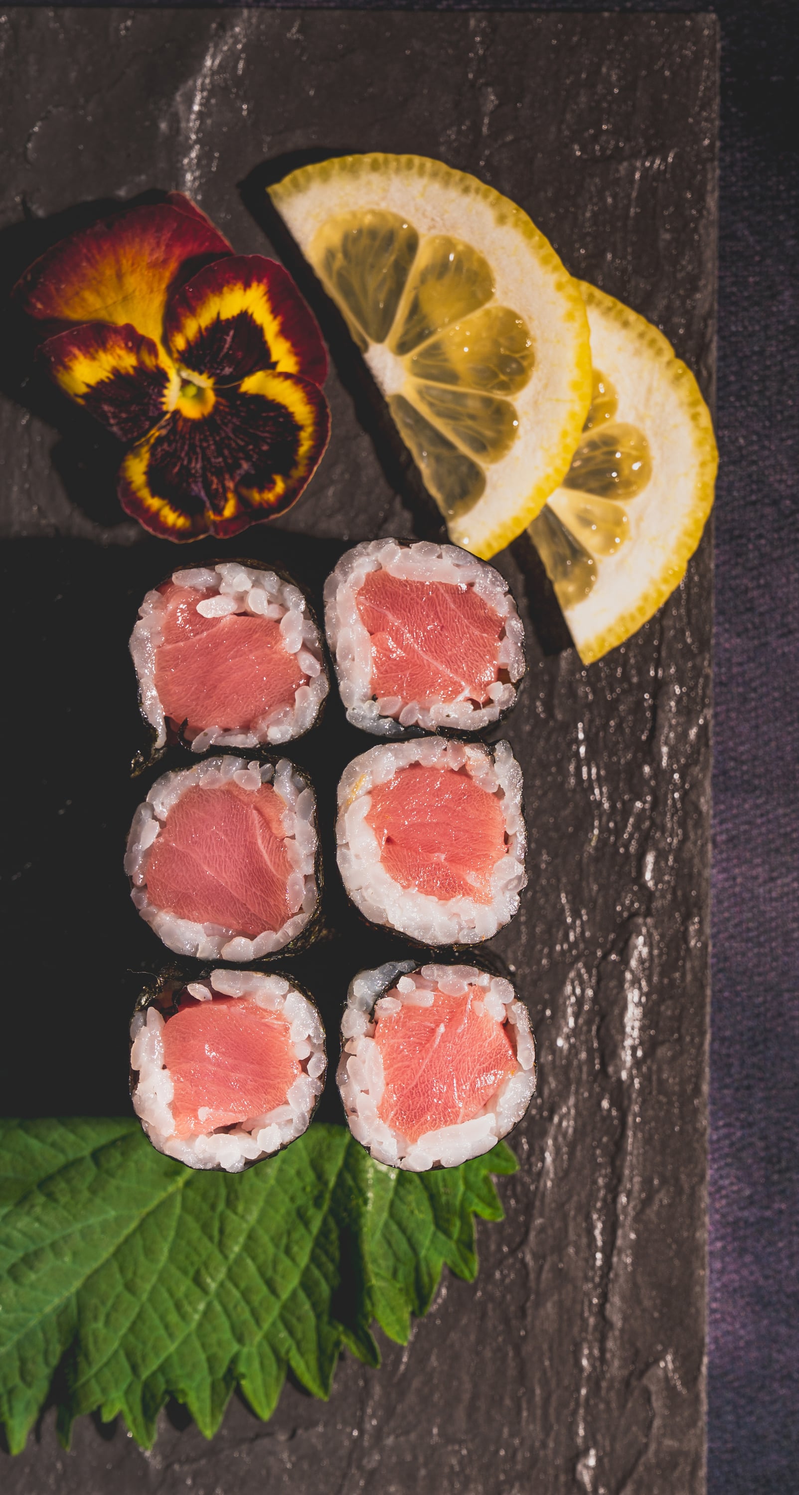 Tuna hosomaki rolls with lemon and pansy on slate