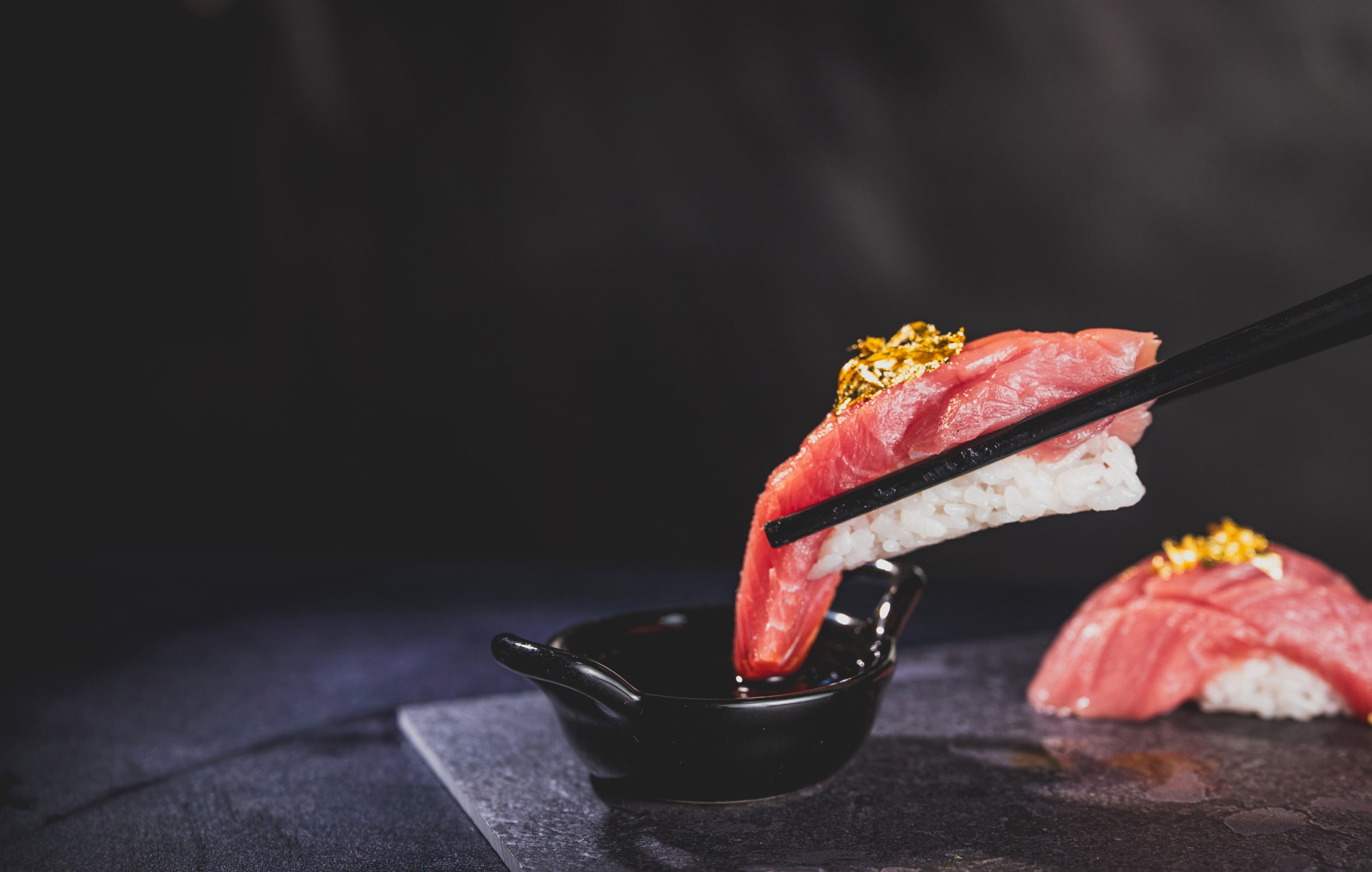 Tuna nigiri with gold leaf held by chopsticks above soy sauce